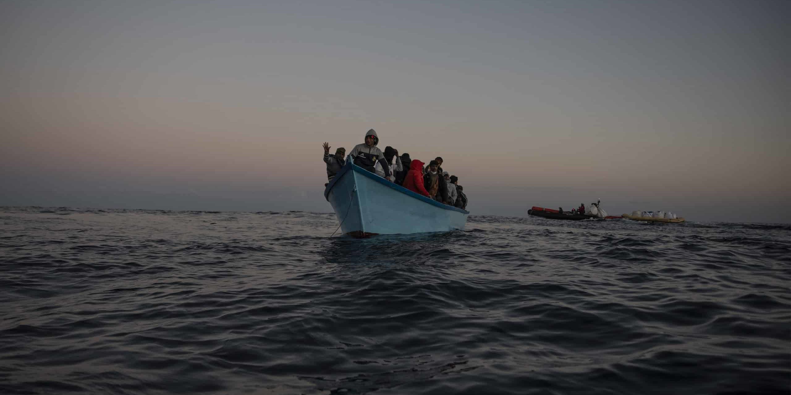 Sea-Watch 5 rettet 50 Menschen, 29.01.2024 50 Menschen auf blauen Holzboot in Seenot. Im Hintergrund ist die Crew der Sea-Watch 5 mit Rettungsausrüstung zu sehen.
