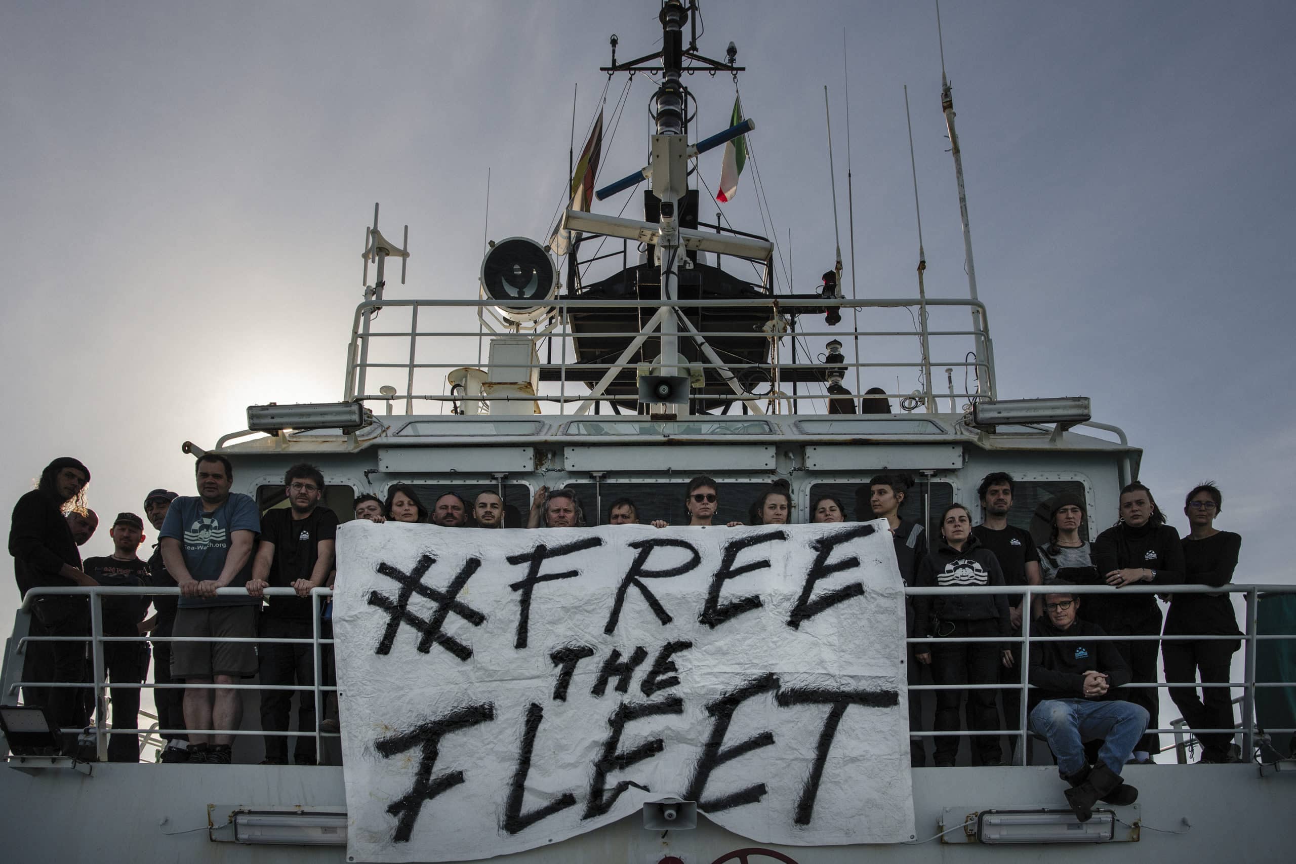 sea-watch schiff mit vielen freiwilligen und banner 'free the fleet'
