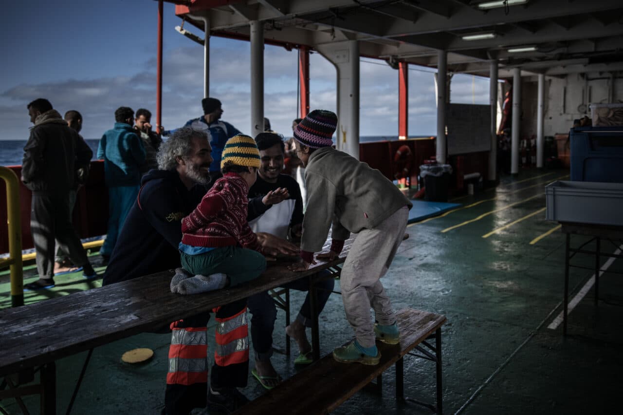 Menschen an Bord der SEA-EYE 4, Kinder spielen mit der Crew, Menschen stehen im Hintergrund