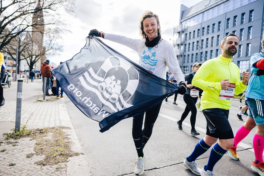 Halbmarathon_Paul Ein Läufer schwenkt bei seinem Spendenlauf auf dem Halbmarathon eine Sea-Watch-Flagge.