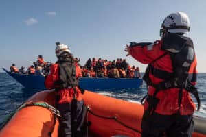 210228_SeleneMagnolia_2284249 Zwei Personen von Sea-Watch befinden sich wenige Meter vor einem Seenotrettungsfall und statten Menschen mit Rettungswesten aus.